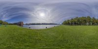 a 360 - camera lens showing the green grass and a large river surrounded by buildings