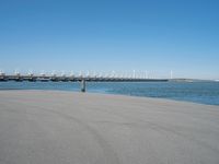 a pier with several wind turbines in the distance next to a body of water with a few boats on it