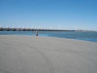 a pier with several wind turbines in the distance next to a body of water with a few boats on it