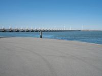 a pier with several wind turbines in the distance next to a body of water with a few boats on it