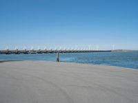 a pier with several wind turbines in the distance next to a body of water with a few boats on it