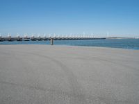 a pier with several wind turbines in the distance next to a body of water with a few boats on it