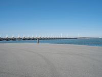 a pier with several wind turbines in the distance next to a body of water with a few boats on it