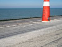 the red and white lighthouse stands on an empty road near a body of water with another ship in the background