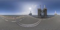 a wide panorama photo taken on a road near a power station and bridge overlooking the ocean