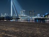 a person riding a bicycle at night near the water's edge and a city bridge