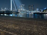 a person riding a bicycle at night near the water's edge and a city bridge