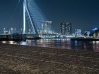 a person riding a bicycle at night near the water's edge and a city bridge