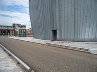 a curved building is near the side of a road, with benches sitting on it