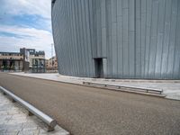 a curved building is near the side of a road, with benches sitting on it