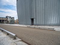 a curved building is near the side of a road, with benches sitting on it