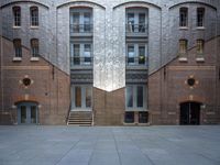 a very big building with an interesting looking window, near some stairs and a brick wall