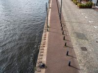 a brick path next to the water with benches on both sides and poles in front of it