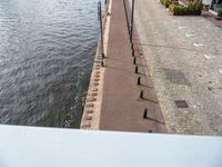 a brick path next to the water with benches on both sides and poles in front of it