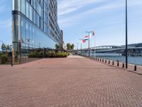 a sidewalk near a large city building next to water and buildings with canadian flags flying