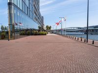 a sidewalk near a large city building next to water and buildings with canadian flags flying