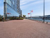 a sidewalk near a large city building next to water and buildings with canadian flags flying