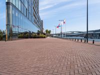 a sidewalk near a large city building next to water and buildings with canadian flags flying