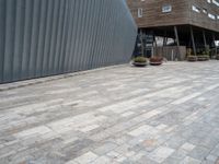 brick walkway next to an industrial building with wood trimming on the wall, and grey cement patio area, near planters and concrete sidewalk area with square seating area