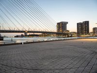 a bridge and an empty pathway beside a river and city skylines in a distance