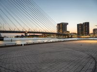 a bridge and an empty pathway beside a river and city skylines in a distance