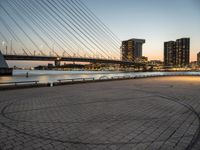 a bridge and an empty pathway beside a river and city skylines in a distance