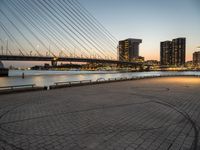 a bridge and an empty pathway beside a river and city skylines in a distance