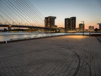 a bridge and an empty pathway beside a river and city skylines in a distance