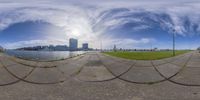 two fisheye photos with a large grassy area near some water and buildings behind them