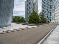 a bench and railing near some tall buildings on a cloudy day / photograph credit j kro