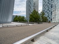 a bench and railing near some tall buildings on a cloudy day / photograph credit j kro