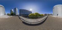 a 360 - view of buildings next to a street near a fence, and the sun is shining on the building