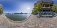 a fish eye view of a brick walkway next to a body of water with some buildings