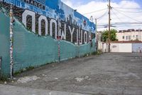 a street corner with a mural in the back, a sign that says hollywood on the side, and a stop sign on the sidewalk