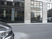 car parked on the side of a street by a tall building with lots of windows