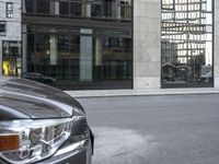 car parked on the side of a street by a tall building with lots of windows