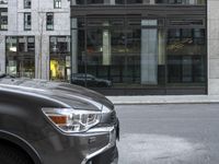 car parked on the side of a street by a tall building with lots of windows