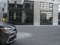 car parked on the side of a street by a tall building with lots of windows