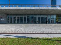 a gray colored concrete building with glass doors and windows and a brick paved walkway on the ground with grass