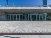 a gray colored concrete building with glass doors and windows and a brick paved walkway on the ground with grass