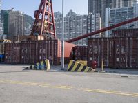 containers and equipment are on the ground near a street with buildings in the background and a crane is lifting them