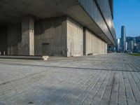 the sidewalk in front of a concrete building near a body of water and some buildings