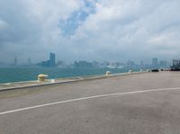 an empty runway by the water with an airplane flying low over it and buildings on both sides