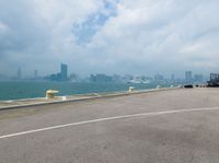 an empty runway by the water with an airplane flying low over it and buildings on both sides