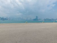 a yellow fire hydrant sitting next to a big body of water with buildings and mountains in the background