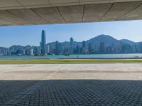 a man sitting down reading under a covered walkway near the beach and mountains in the distance