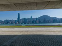 a man sitting down reading under a covered walkway near the beach and mountains in the distance