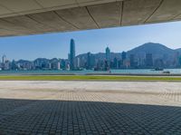 a man sitting down reading under a covered walkway near the beach and mountains in the distance