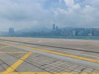 a parking lot near the water at an airport with buildings in the background and a plane on the runway