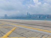 a parking lot near the water at an airport with buildings in the background and a plane on the runway